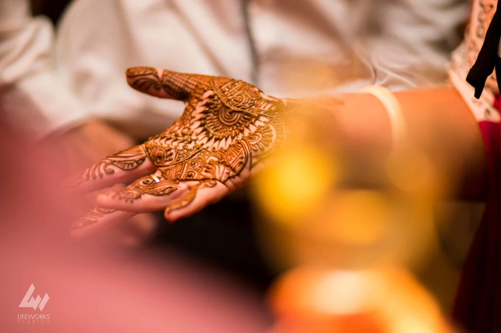 A close-up image of a guest's hands adorned with beautiful, intricate Mehendi designs, showcasing traditional patterns and delicate details.