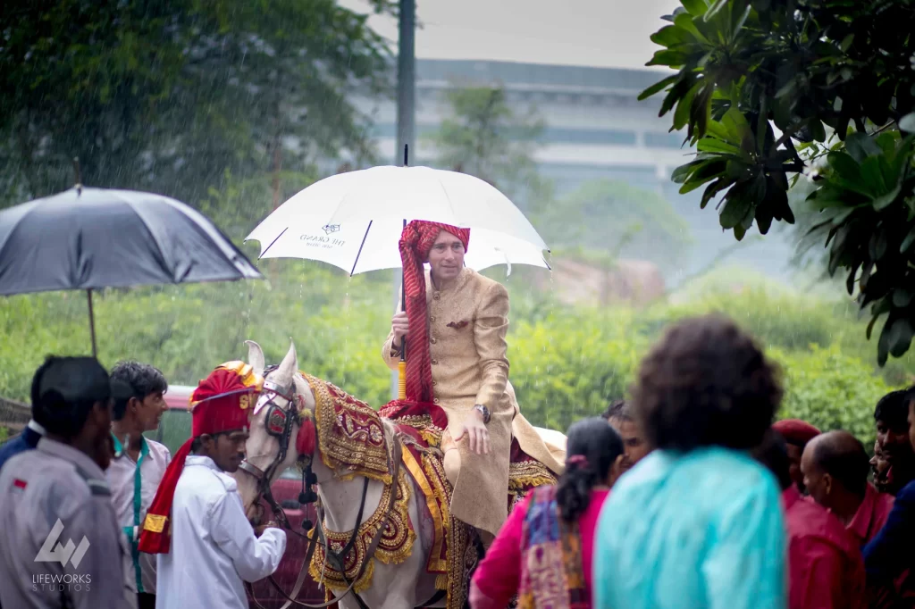 An image of the groom mounted on a majestic horse carrying umbrella, exuding regal poise and traditional flair, symbolizing grace and grandeur in the context of a wedding celebration.