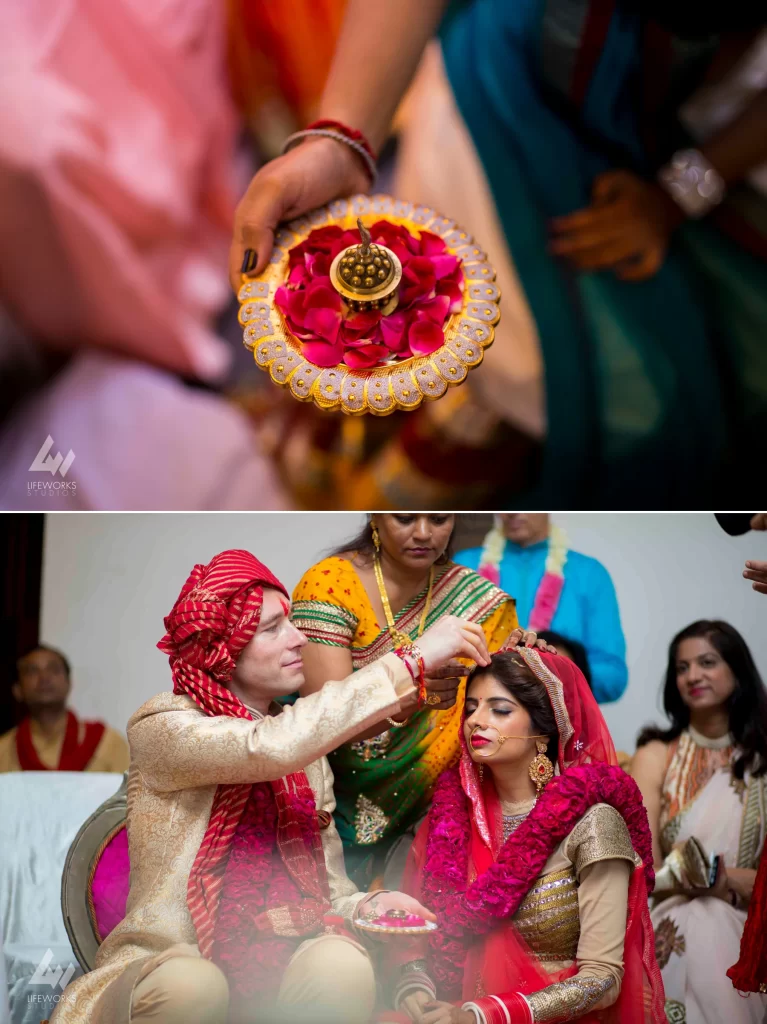 A close-up image of the groom delicately applying sindur (vermilion) to the parting of the bride's hair, symbolizing the sacred bond of marriage in Hindu tradition.