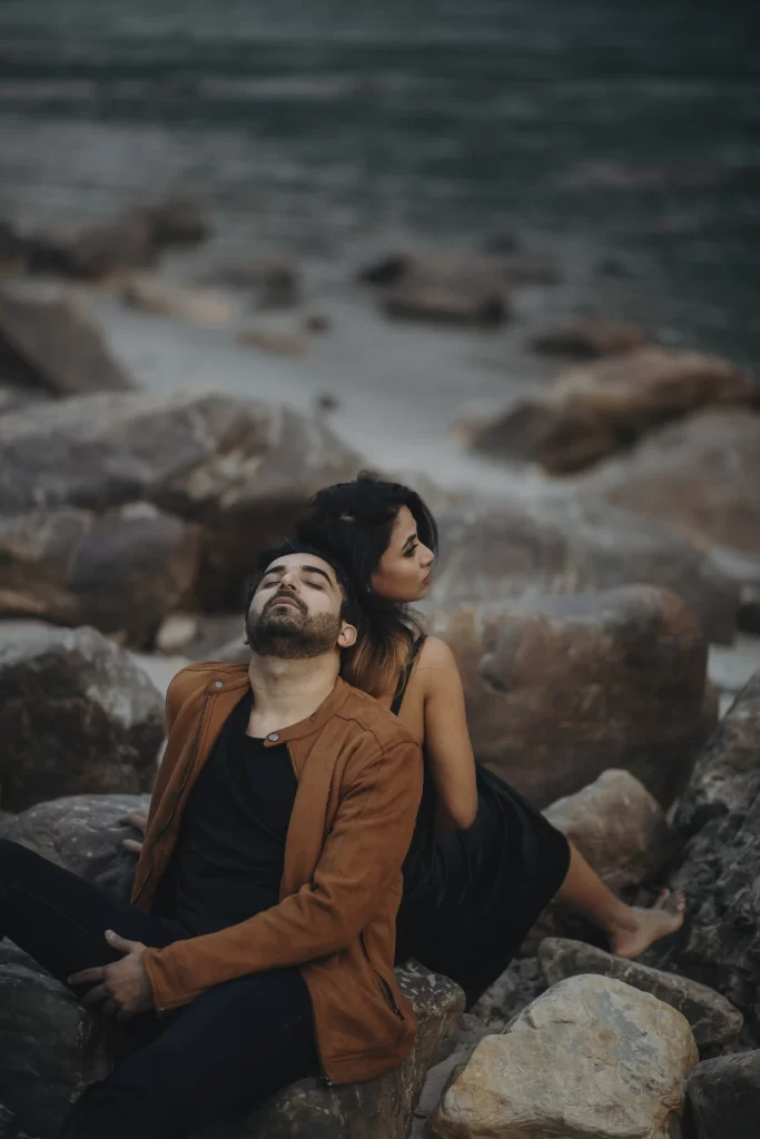 A couple sits on a rock, each facing away from the other, gazing in opposite directions, evoking a sense of contemplation and individual reflection in the midst of nature's tranquility.