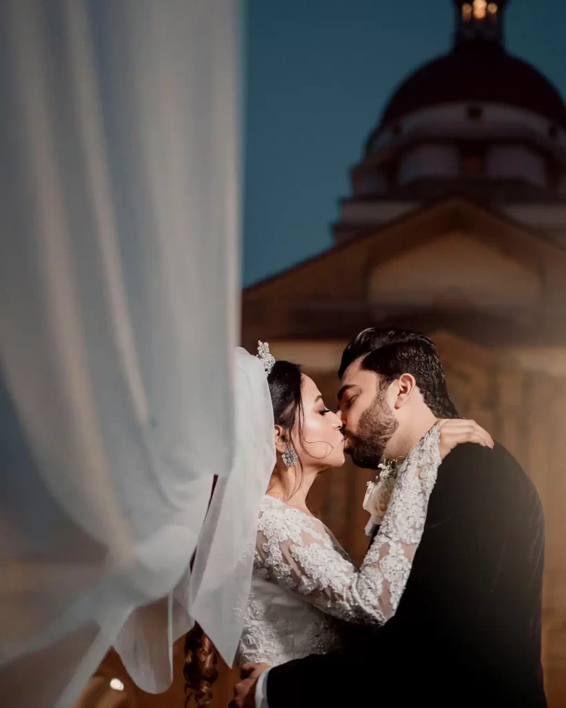 A happy couple sharing a romantic kiss outside a church in Delhi after their wedding ceremony, surrounded by blooming flowers and joyful guests.