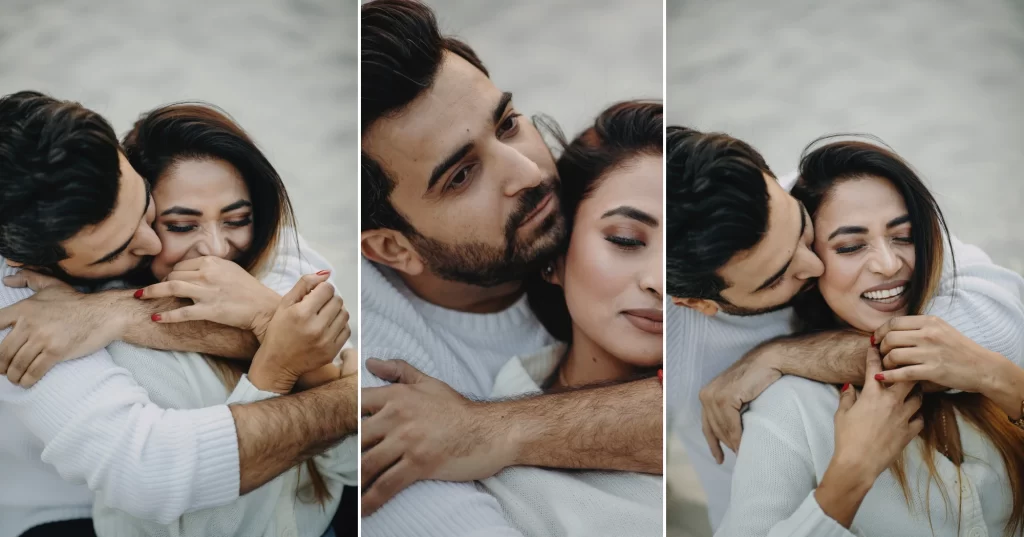 A groom wearing a Jeans and sweatshirt embraces a bride from behind in a pre-wedding photo shoot. The bride is wearing a white dress and both are smiling.