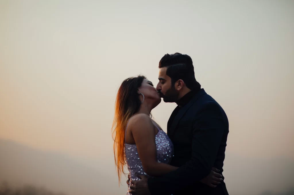 A beautifully composed image capturing a couple sharing a tender kiss against the backdrop of a breathtaking sunset. Their embrace reflects deep affection and romance, set against the serene and vibrant hues of the setting sun, creating a timeless, romantic moment.