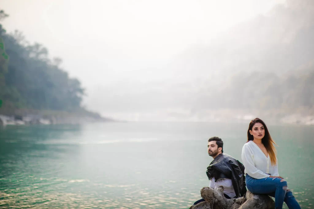 A serene image of pre-wedding shoot in rishikesh portrays a couple seated on a rock near a river, surrounded by breathtaking natural scenery. The couple's relaxed posture and peaceful surroundings evoke a sense of tranquility and togetherness, creating a timeless moment in the pre-wedding shoot.