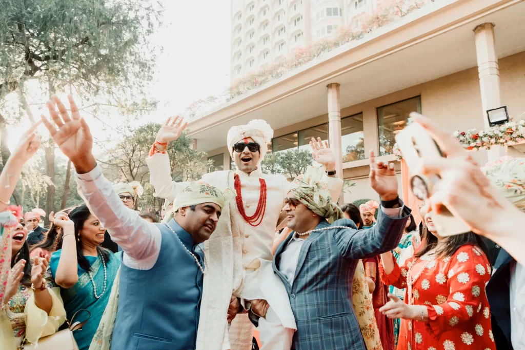 An Indian groom joyously dancing in traditional attire, expressing celebratory movements amidst vibrant cultural decor and music.