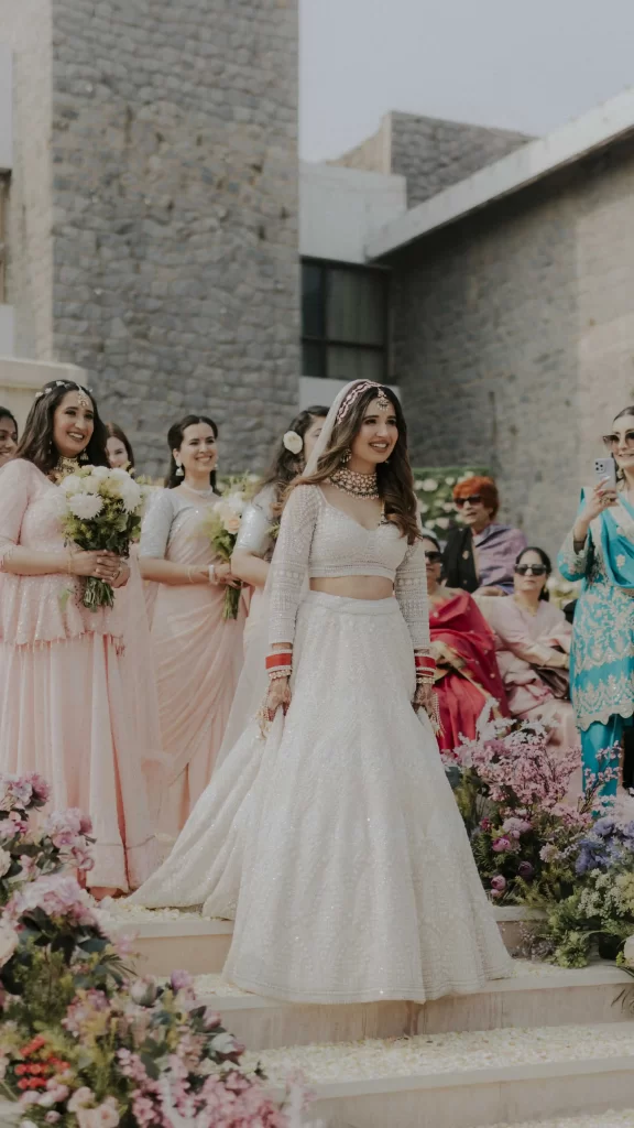 The bride walks down the aisle escorted by her bridesmaids, exuding elegance and joy on her special day.