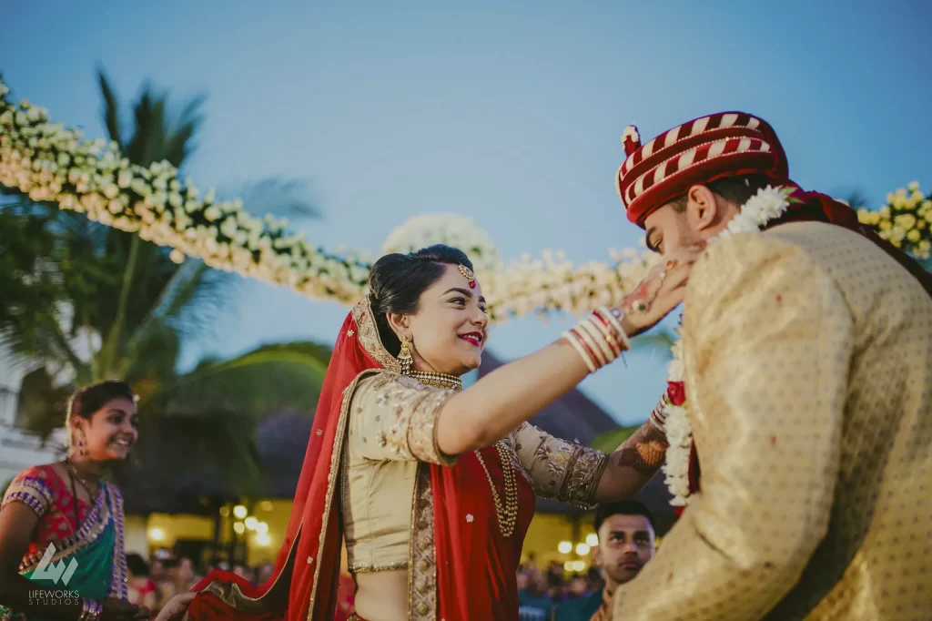 A joyful couple exchanging varmala garlands, adorned with vibrant flowers, at a traditional Indian wedding.