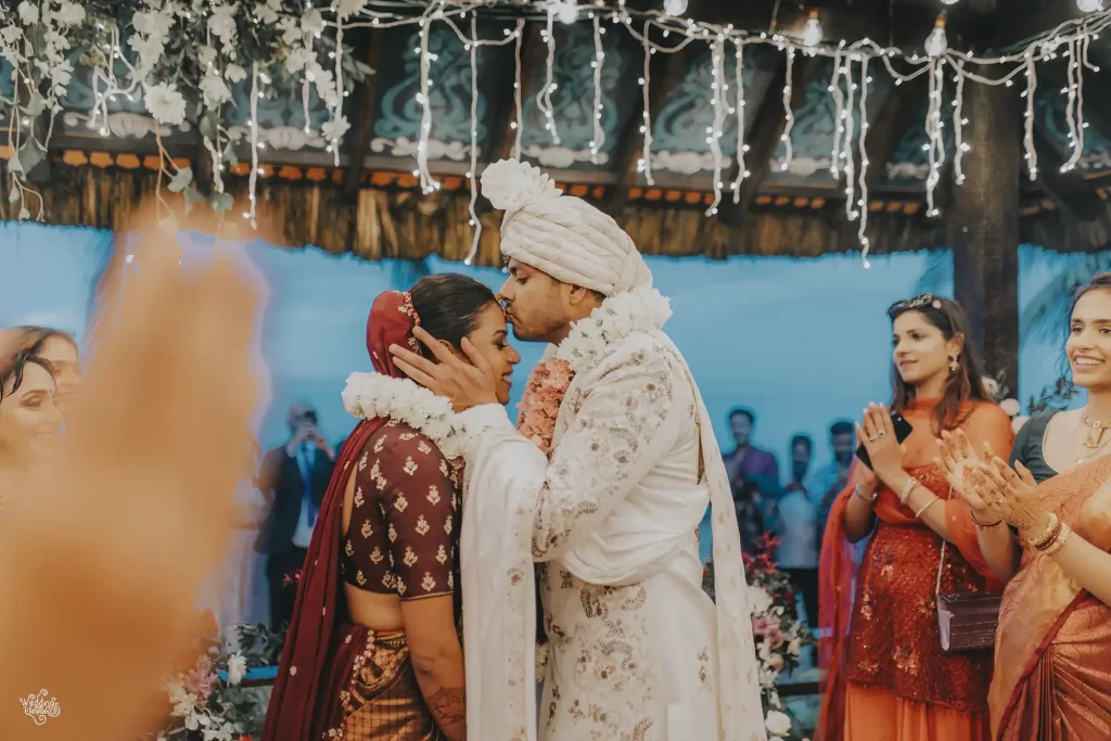 Groom affectionately kisses the bride on her forehead after the varmala ceremony, symbolizing love and respect in Indian wedding tradition.