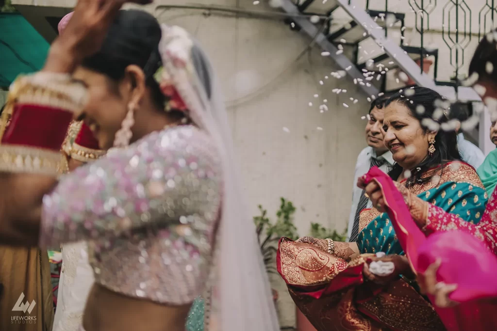 A bride in traditional attire playfully tossing rice puffs as family members joyfully collect them in their sarees during a 'bidaai' ceremony, capturing a lighthearted and auspicious tradition in Indian weddings.