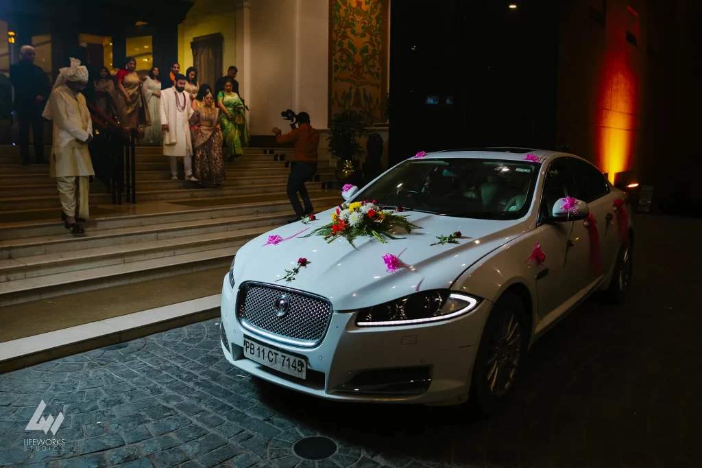 A newlywed couple in traditional attire walking towards a car, symbolizing the emotional moment of 'bidaai' in Indian culture."