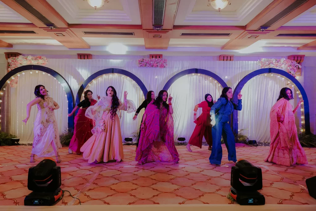  During the lively sangeet ceremony, the bride dances joyfully with her friends, celebrating in an atmosphere filled with happiness and energy.  