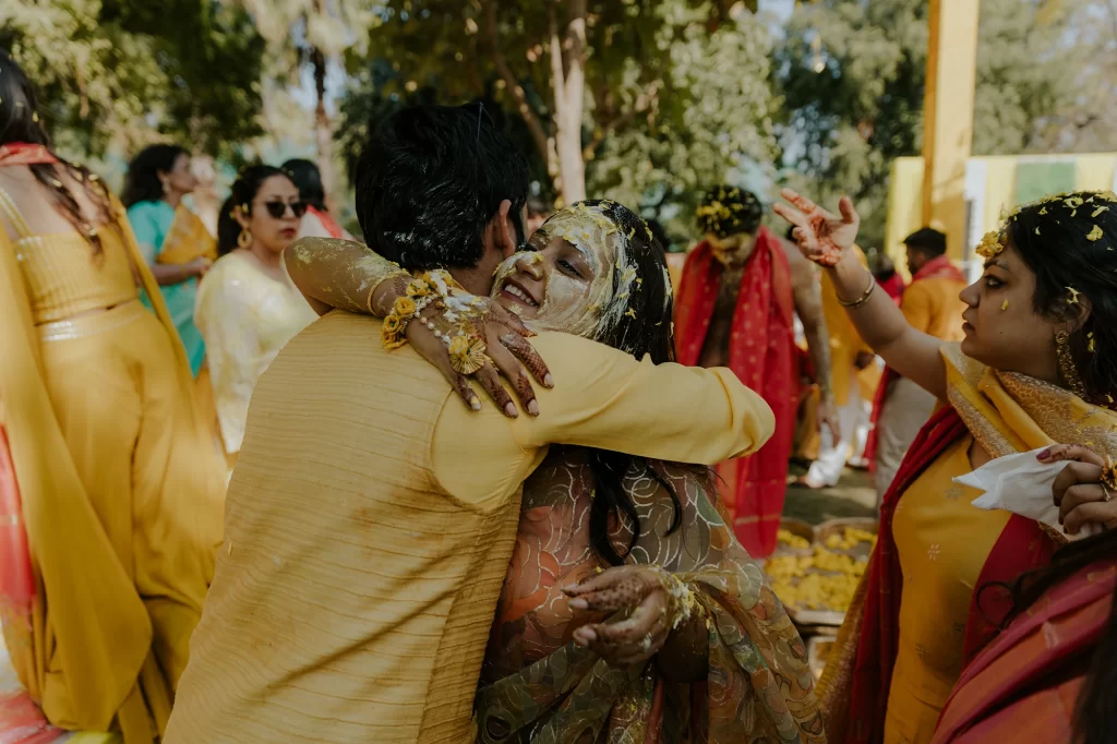 Embracing blissfully, the bride and groom share a warm hug post applying haldi at their joyous and colorful haldi ceremony.