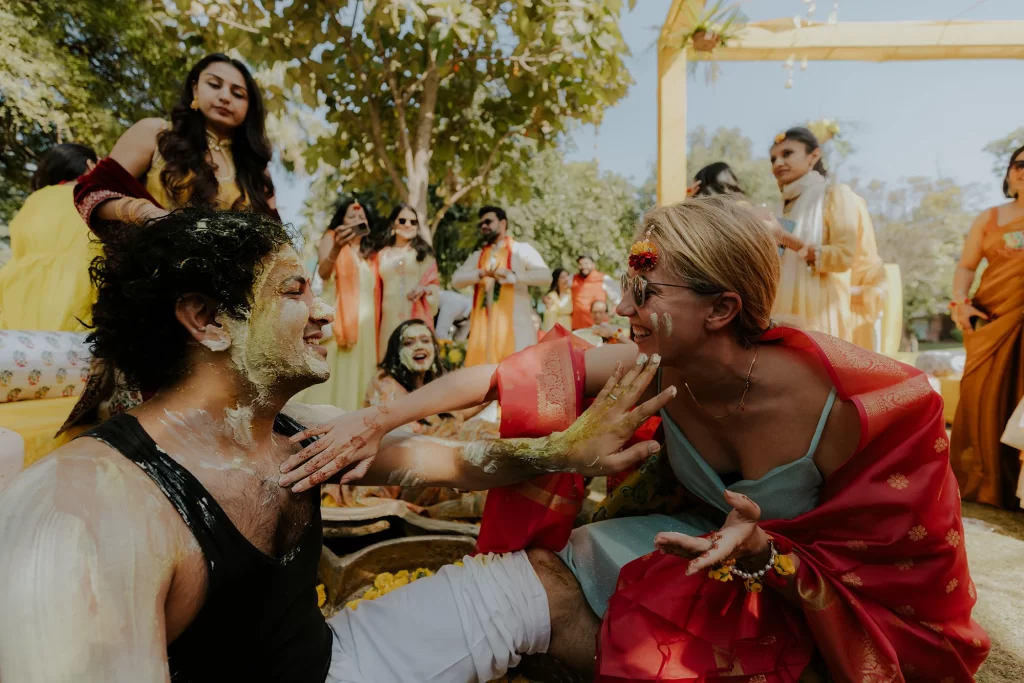  During the haldi ceremony, the groom's friends joyfully apply haldi to the groom, fostering an atmosphere of celebration and camaraderie.  