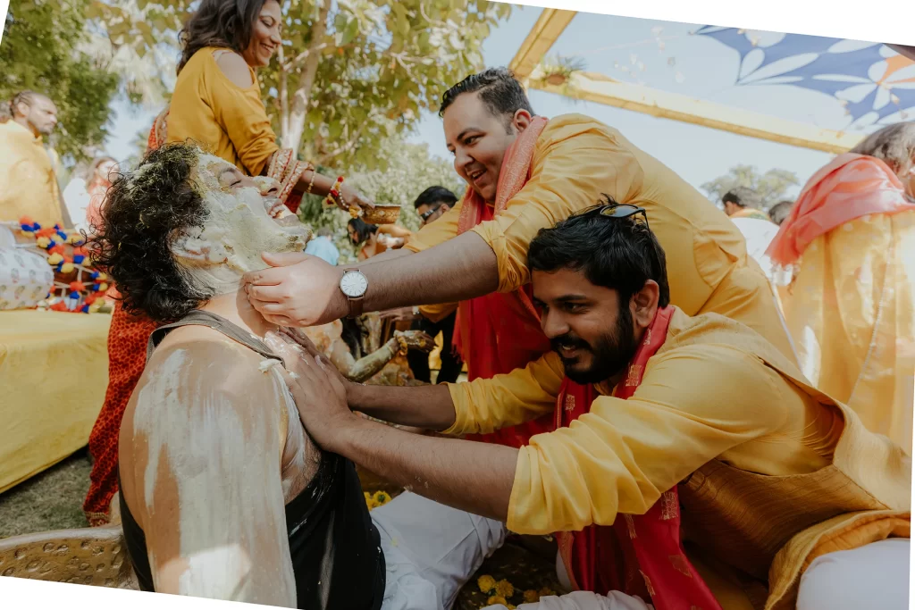  During the haldi ceremony, the groom's friends joyfully apply haldi to the groom, fostering an atmosphere of celebration and camaraderie.  