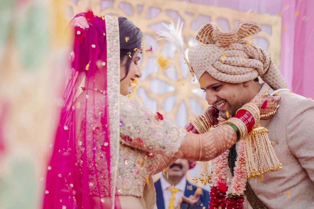 Vibrant varmala ritual at The Grand, Delhi, highlighting the couple joyfully exchanging garlands in a lavish destination wedding setting.