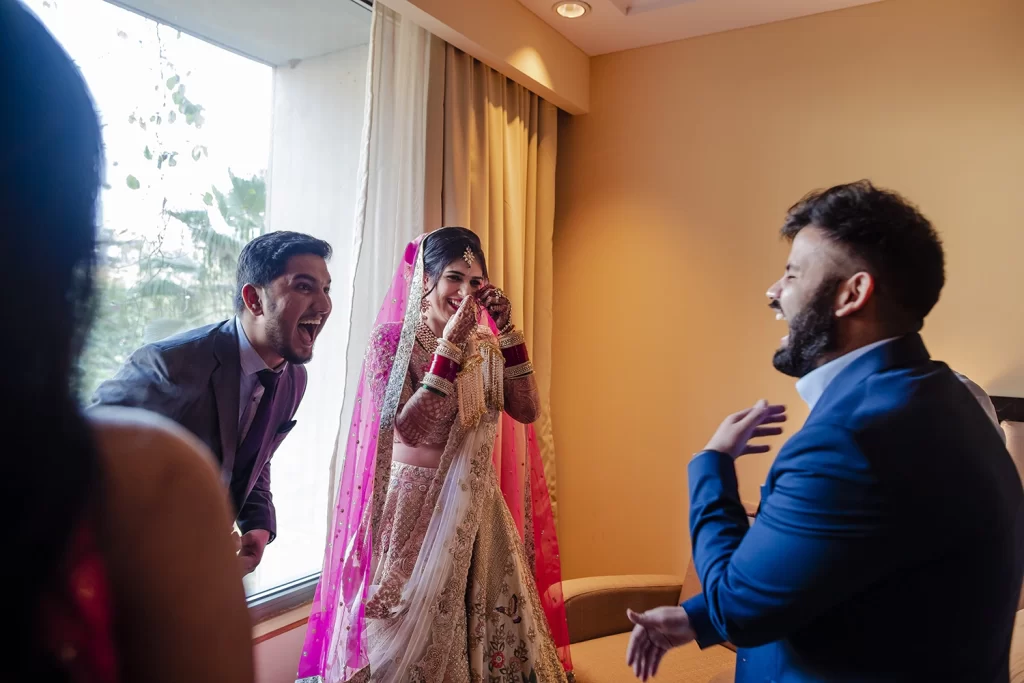 Indian bride laughing with her brother, friends, and sister, celebrating joyfully after preparing for her wedding.