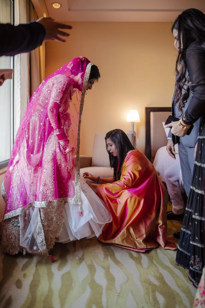 A loving sister assists the bride in arranging her vibrant lehenga, ensuring every detail is perfect for the wedding day.