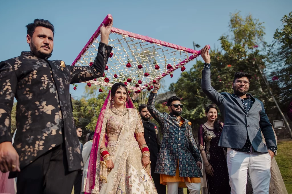 Bride, under a floral canopy held by her brothers, walks gracefully to the mandap, a moment of familial love and tradition.