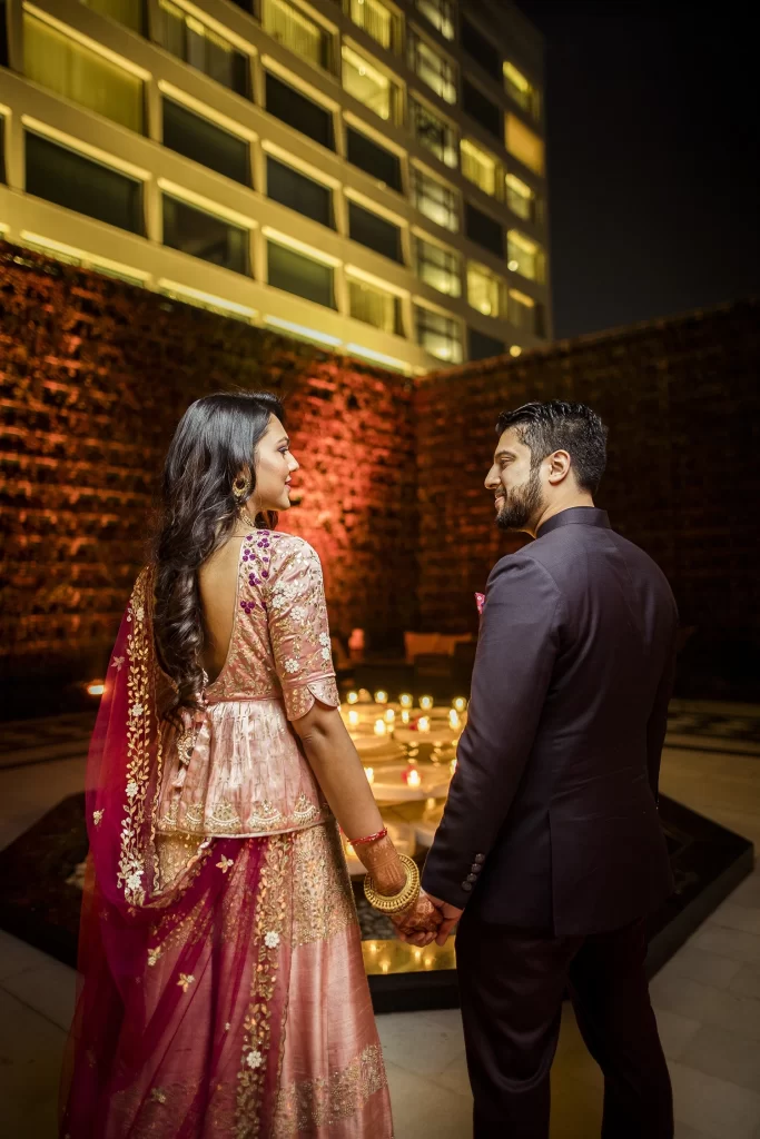 A couple standing in a candid moment at The Oberoi, Delhi, captured in a romantic embrace, smiling and happy.