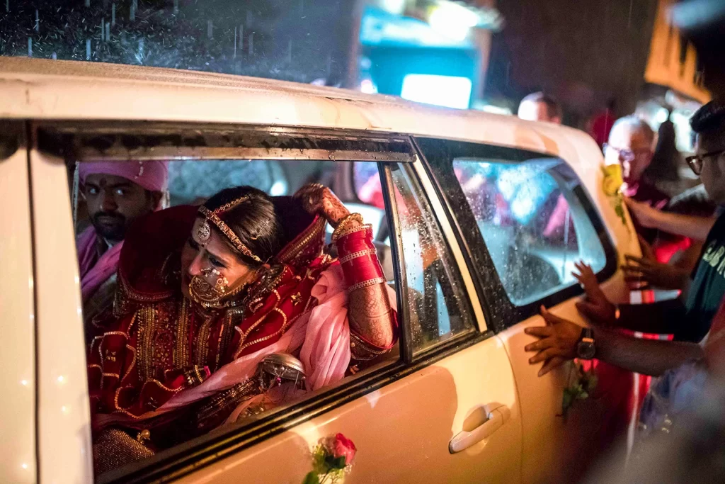 A bride, holding her bidai, sits with tears in her eyes, expressing emotions as she prepares to leave her parental home.