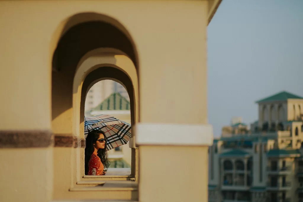 A bride in a wedding attire standing on a balcony at a wedding venue, looking out with a radiant smile.