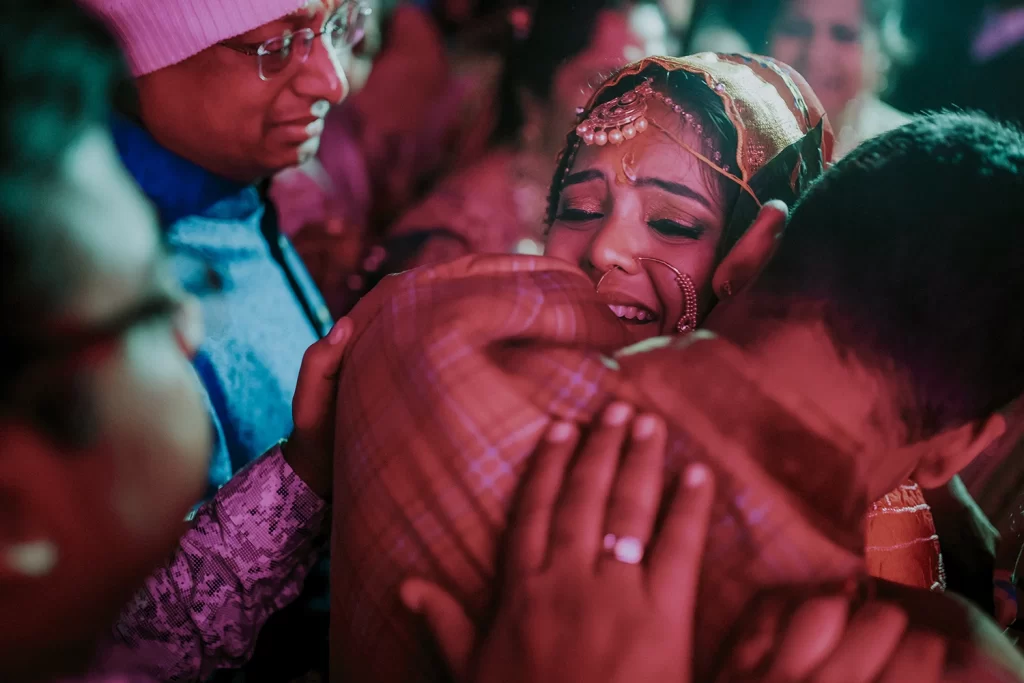 A bride in bridal attire embraces her brother tenderly during her bidai ceremony, capturing a heartfelt moment of love and departure.