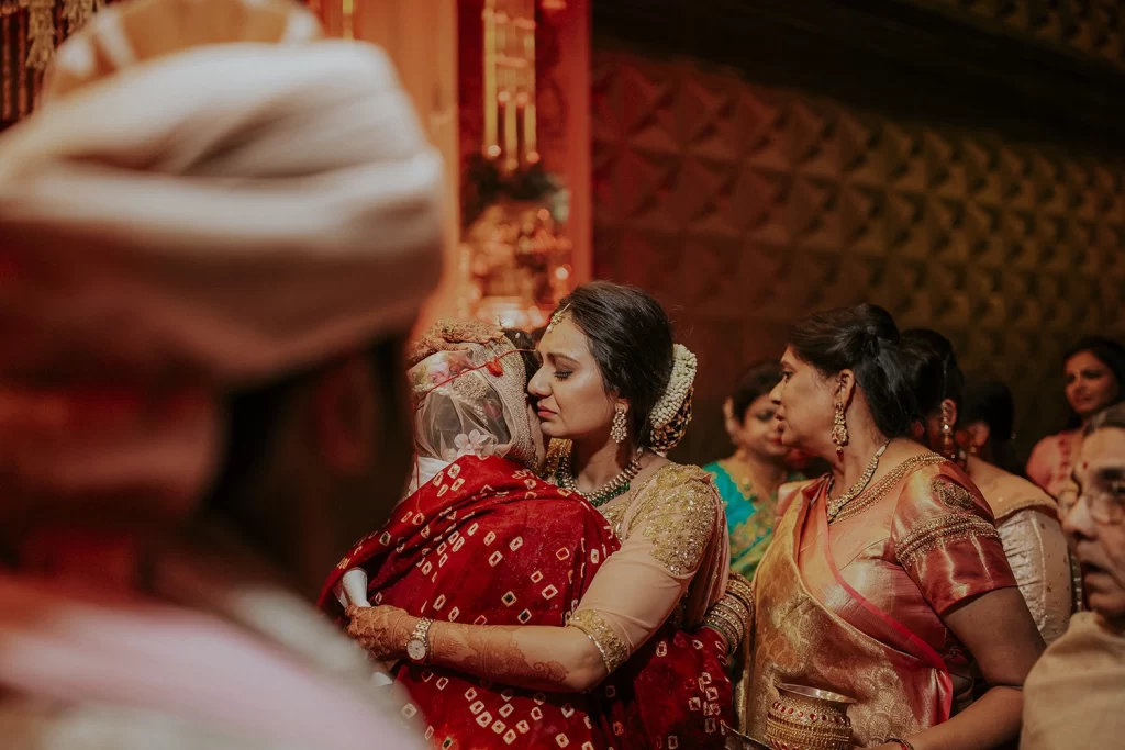 A bride in bridal attire embraces her mother tenderly during her bidai ceremony, capturing a heartfelt moment of love and departure.