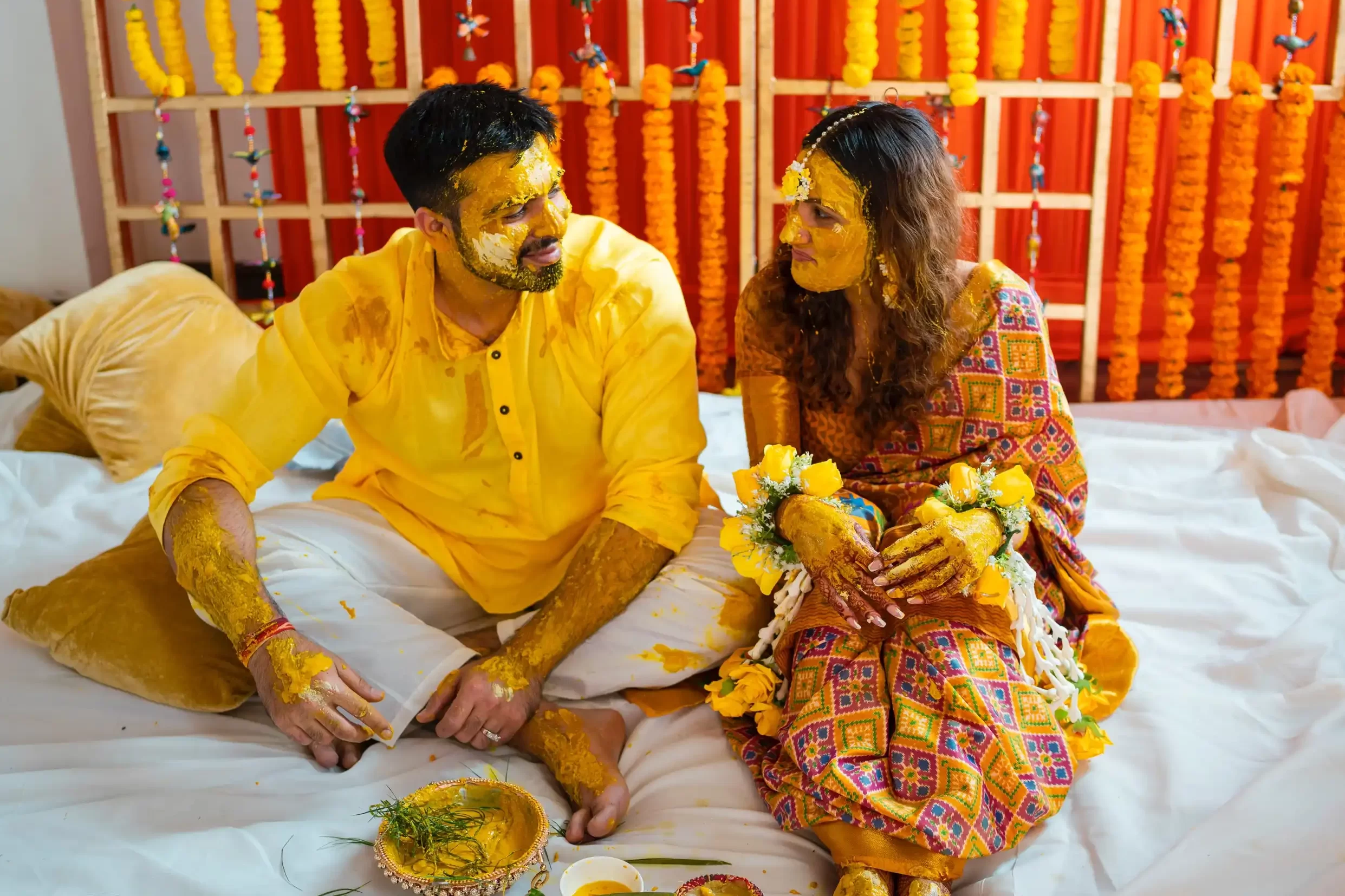 Groom and bride's haldi ceremony, both beams with joy as turmeric paste is applied traditionally.