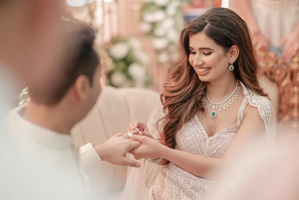 The groom slips an engagement ring onto the bride's hand, symbolizing their commitment and love during the engagement ceremony.