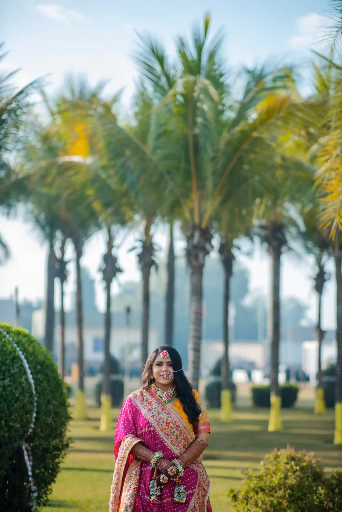 A joyful bride-to-be sitting surrounded by vibrant yellow turmeric paste and flowers, getting ready for her haldi ceremony.