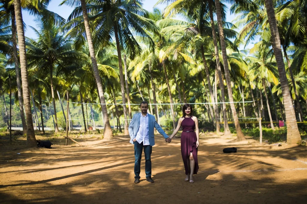 Couple holding hands and surrounded by palm trees during their pre-wedding shoot in Goa.