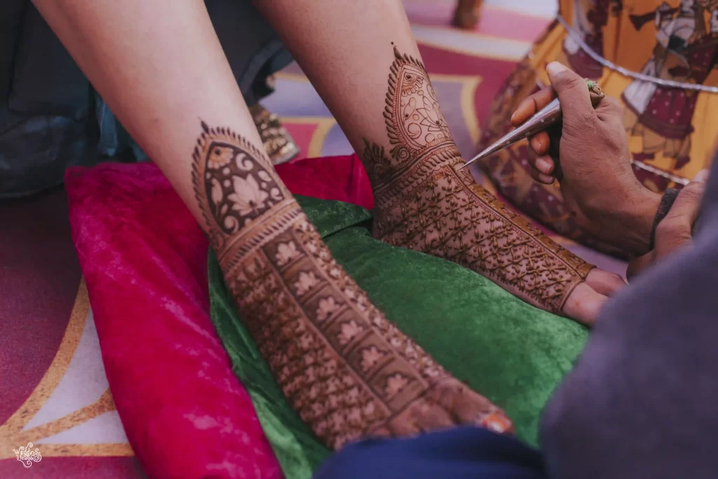 A close-up of mehndi patterns on feet, featuring elaborate designs that complement the bride's outfit.