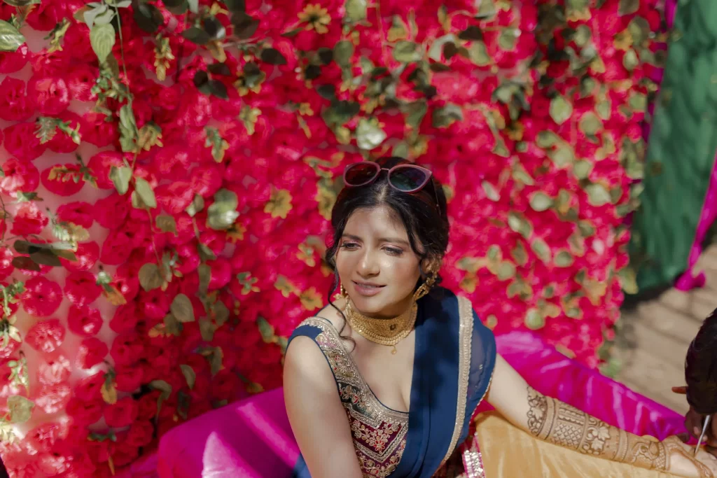 An elegant mehndi decoration featuring colorful drapes, floral arrangements, and twinkling lights at a wedding venue.