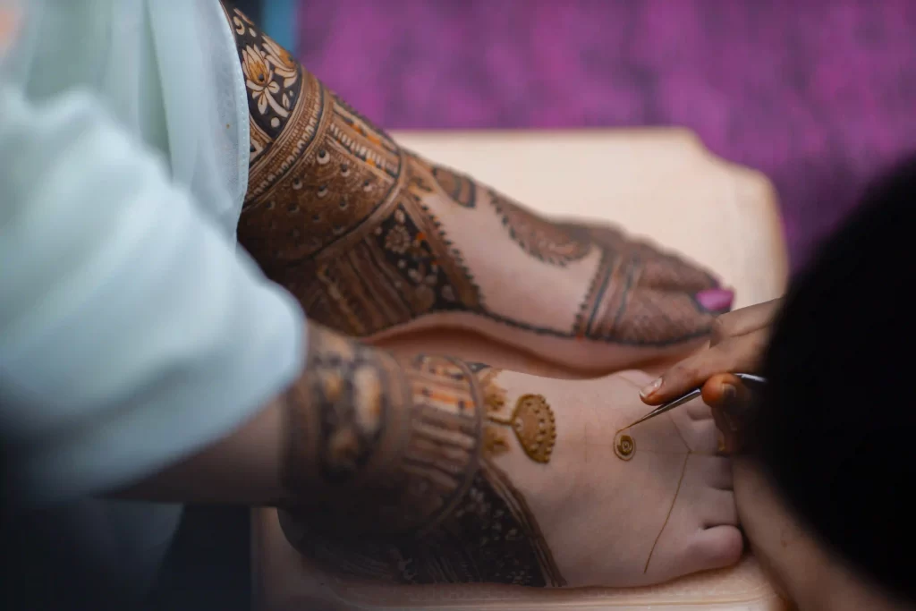 The bride getting intricate mehndi designs applied to her legs.