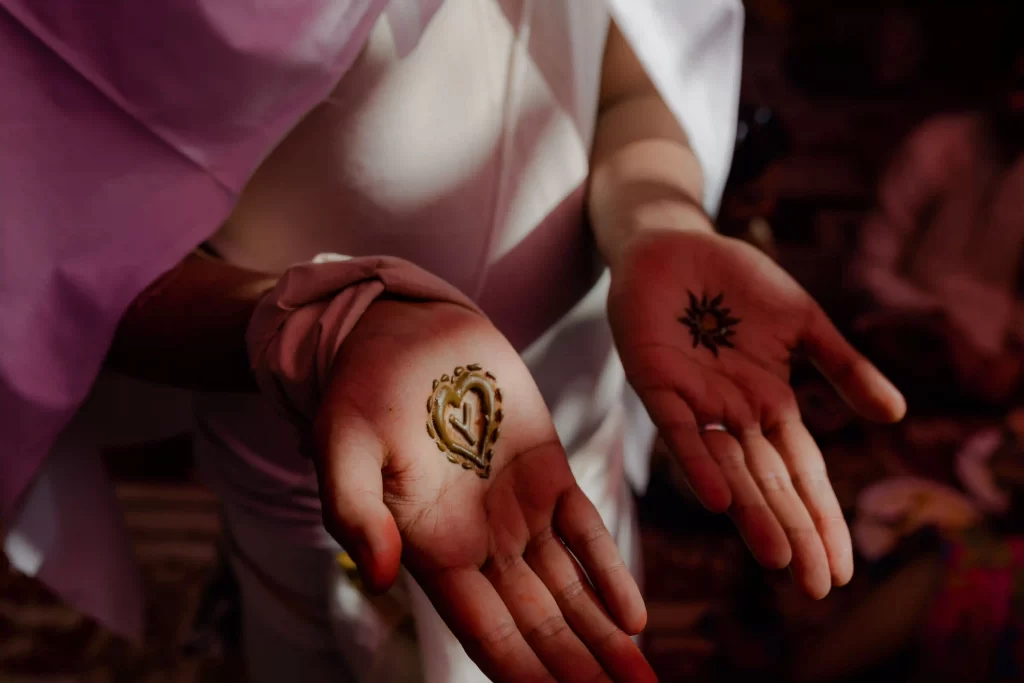 Groom proudly displays the bride's name initials written on his palm, surrounded by the joyful atmosphere of Mehndi songs for wedding.