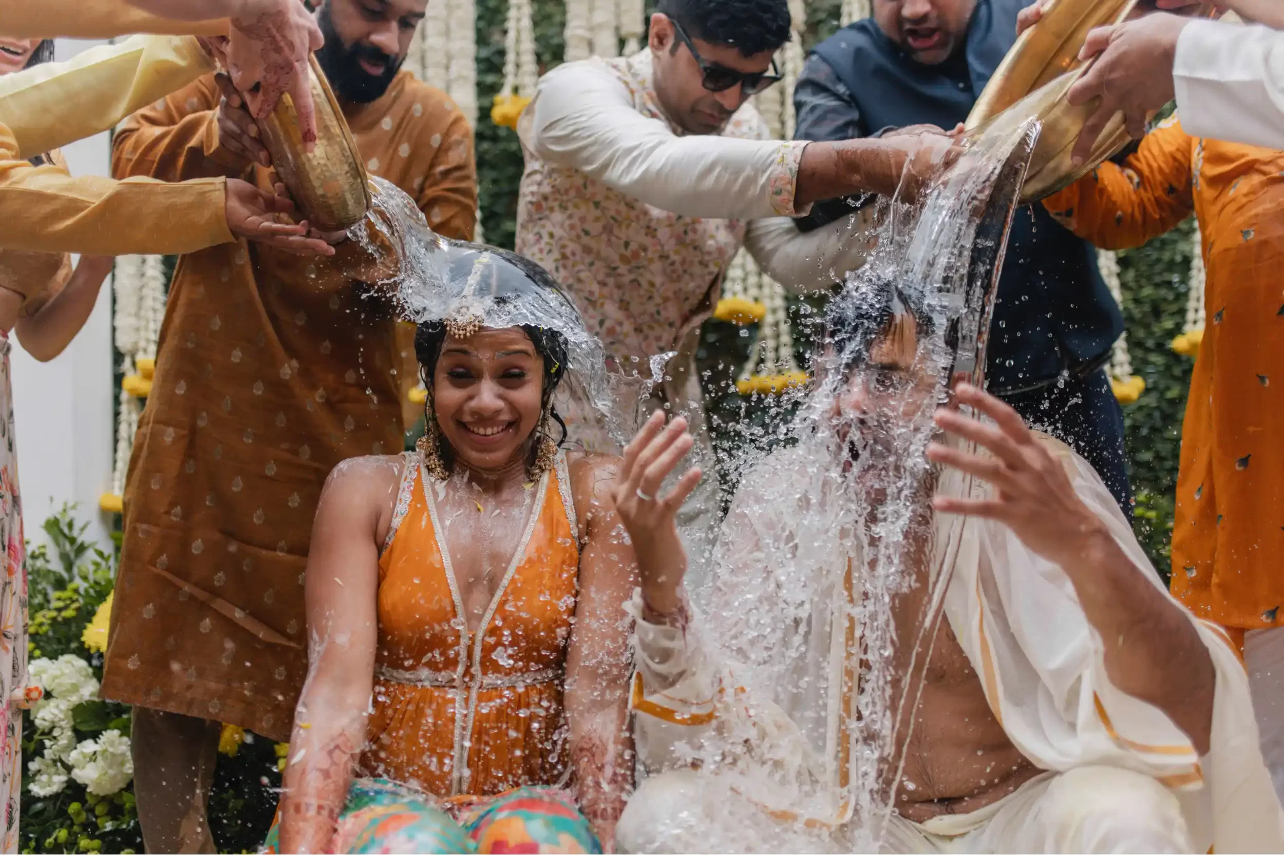 In a colorful Hindu wedding in Dubai, friends joyfully throw water at the bride and groom during the festive haldi ceremony.